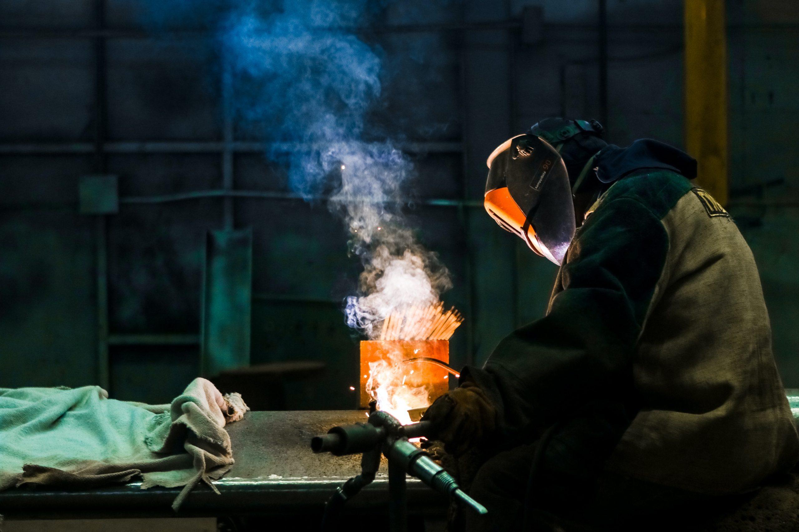 Bild eines Arbeiters mit Schutzkleidung und Metallmaske während er Schweißarbeiten durchführt. Beispielbild für die Metallrente in der Stahlindustrie.