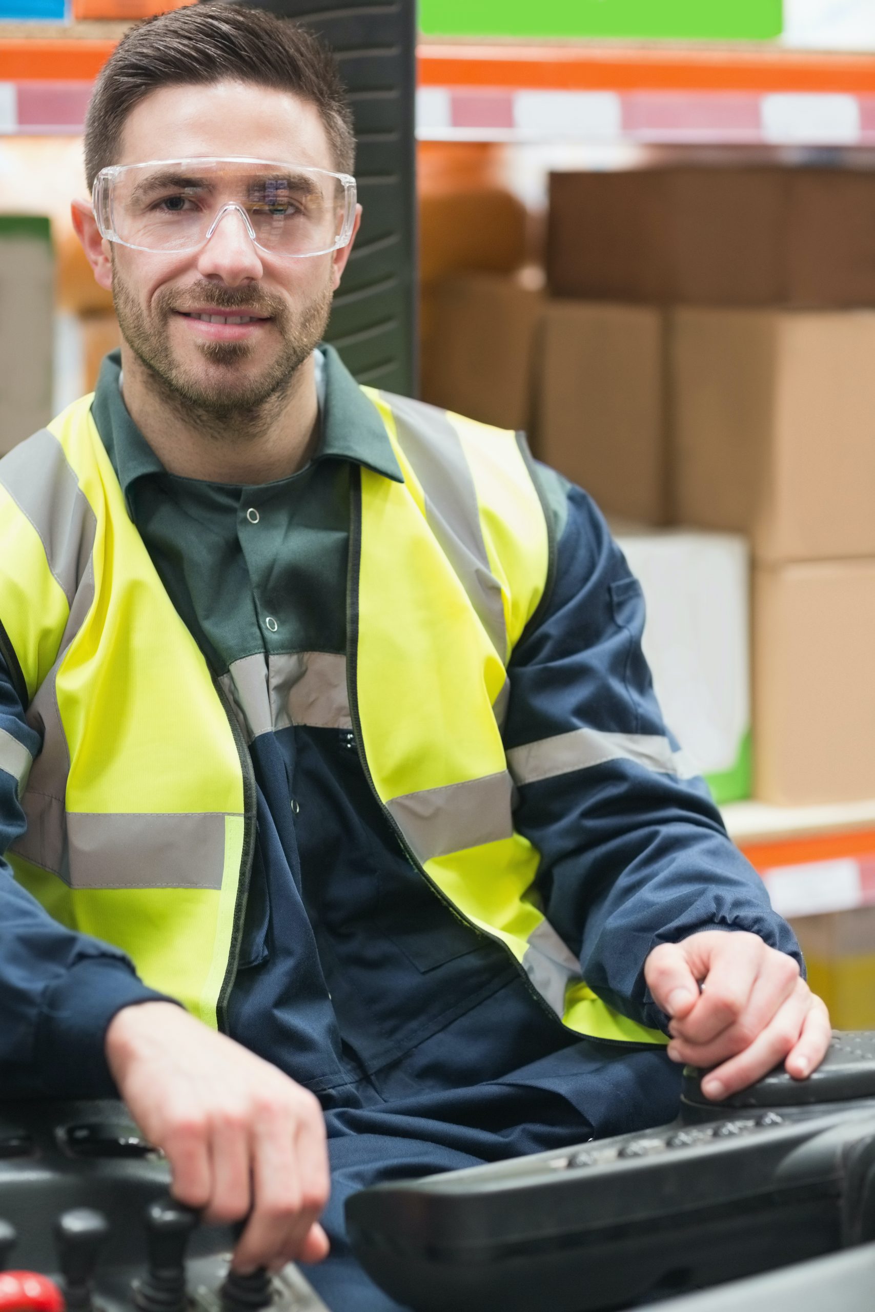 Bild eines lächelnden Arbeiters mit Schutzbrille und -weste auf einem Gabelstabler.