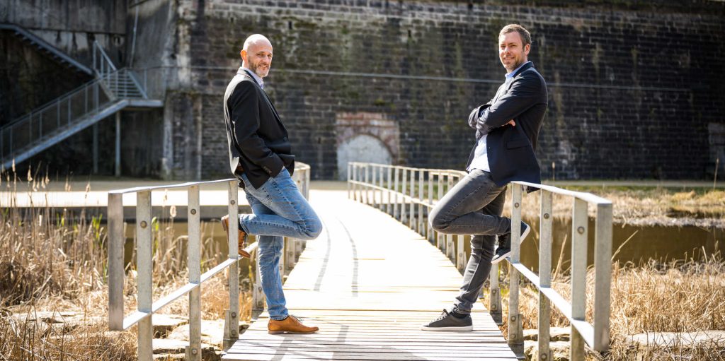 nexuro Versicherungsmakler Tobias Schmidt und Patrick Palz in der Natur auf einer Brücke in Farbe